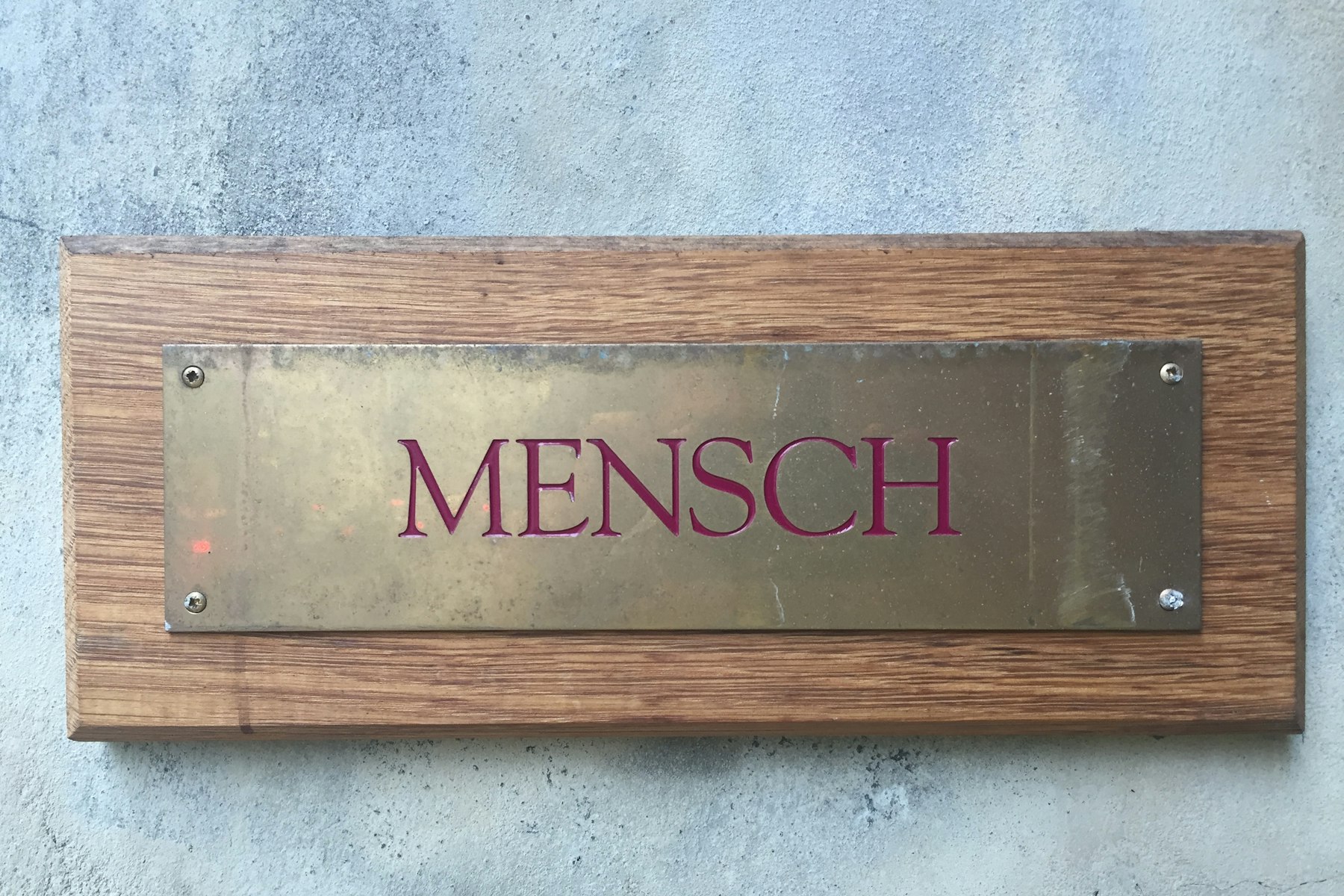 A brass company nameplate mounted on a wall beside an entrance