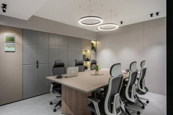 A meeting room with a long table, ring pendant lights and seating for eight