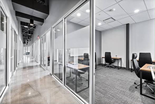 A corridor of glass-fronted private offices, each with a desk and chairs